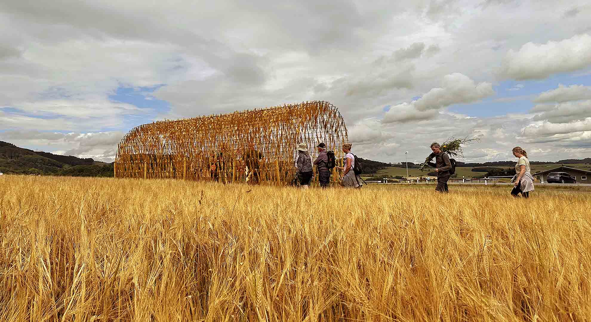 Straw pavilion blending with a wheat field, demonstrating architecture’s role in conserving resources through natural materials.