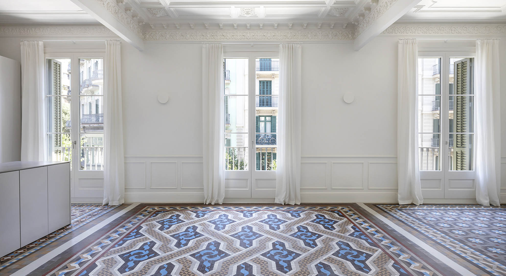 Restored modernist apartment in Barcelona featuring original mosaic floors and decorative ceilings, highlighting historical building materials.