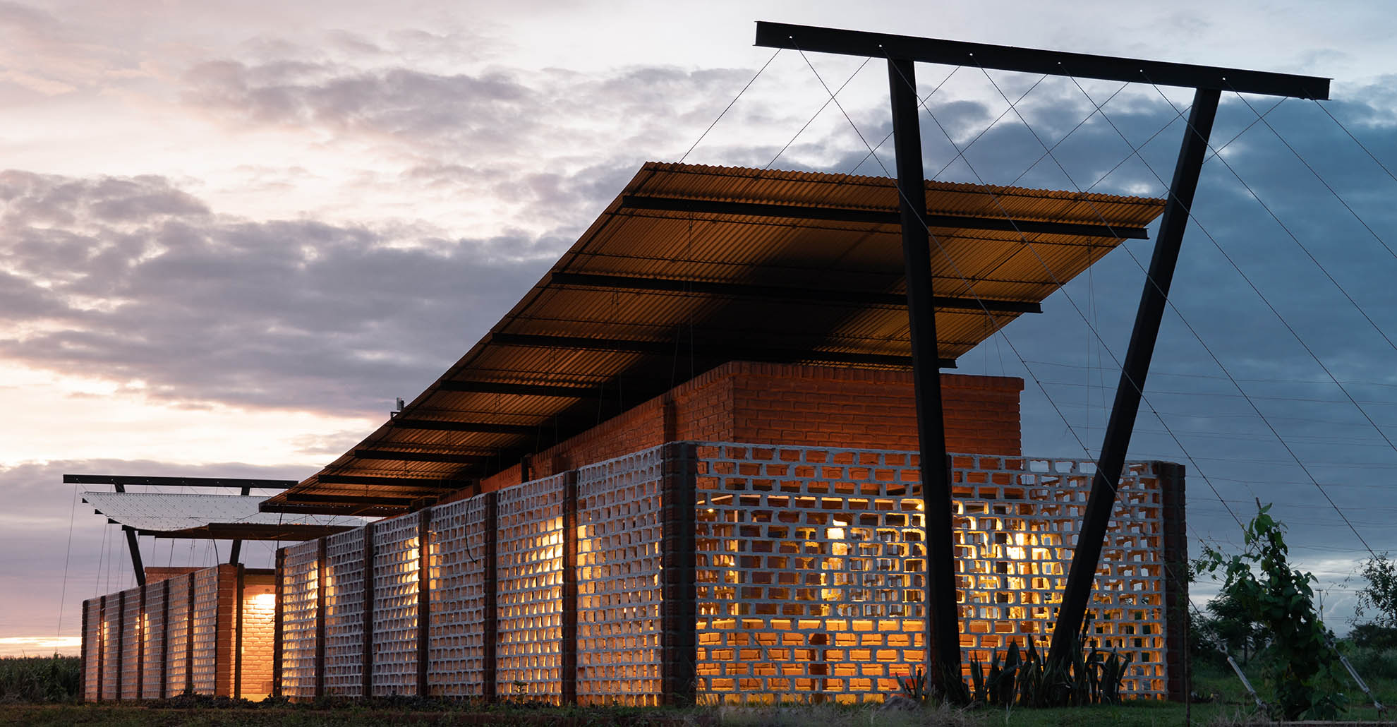 Illuminated facade of Oficina Nordeste Curuguaty, showcasing the reuse of soil bricks and passive strategies.