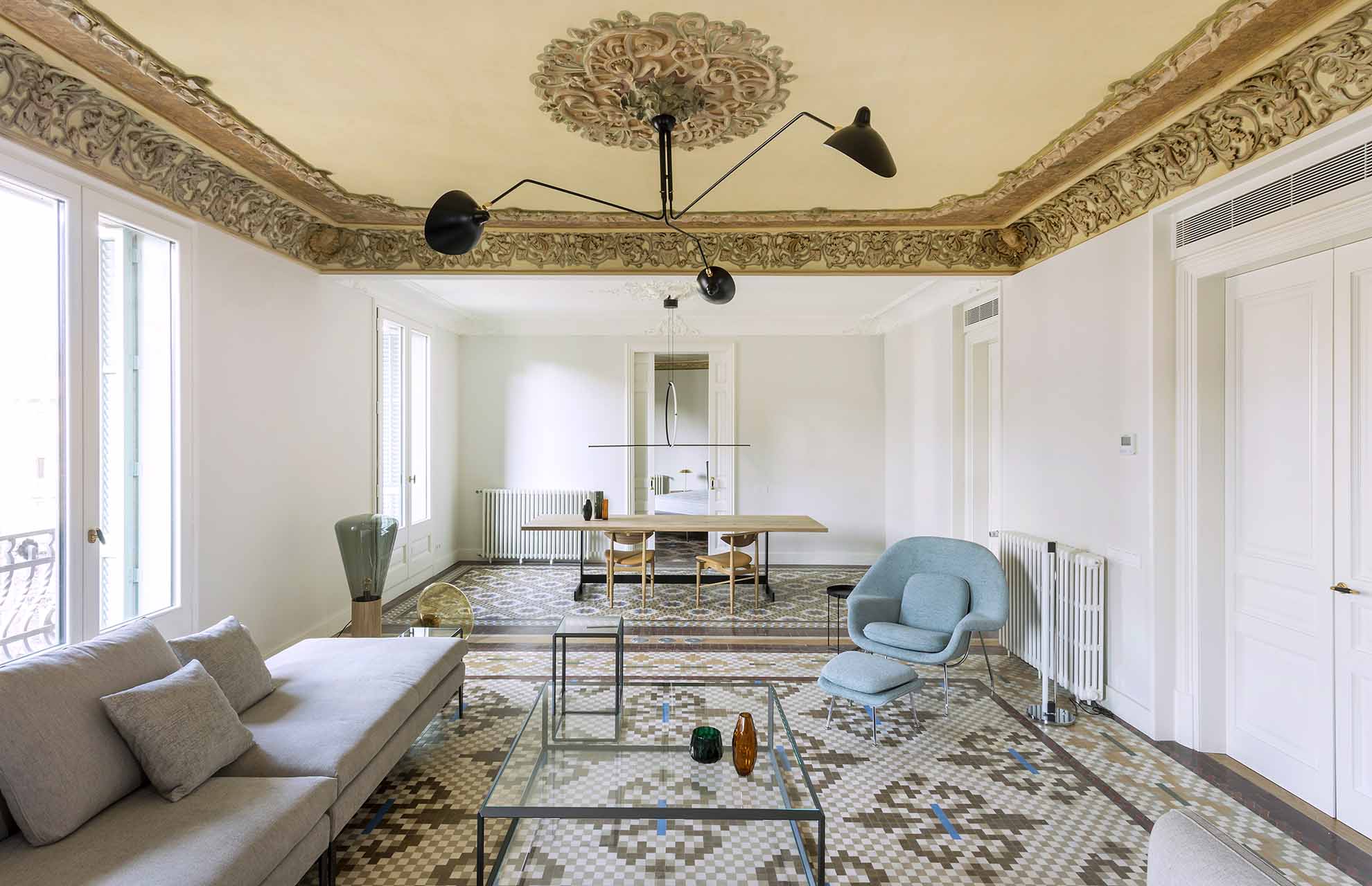 Elegant living-dining area in a restored Barcelona apartment, preserving original ceilings and mosaic floors as key building materials.