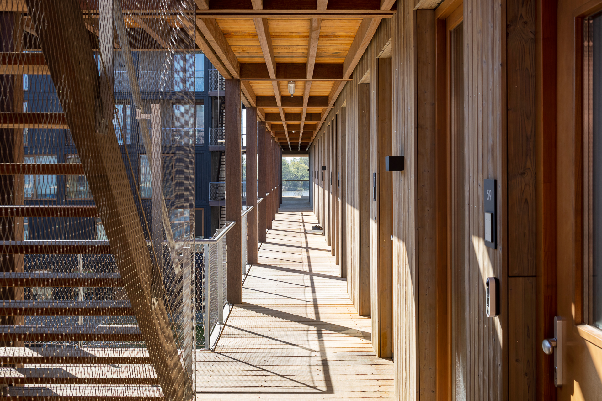 Wooden corridor and apartment entrances at Juf Nienke, an example of sustainable housing with circular architecture.